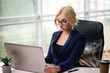 © ostap_davydiak - smiling blonde businesswoman with glasses using laptop in the office