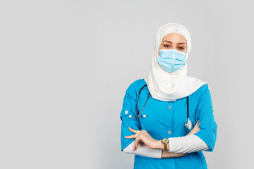 Wall Mural -  friendly Muslim doctor or nurse wearing hijab and medical face mask and gloves on a gray background.