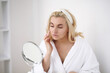 © ostap_davydiak - Young woman with flawless skin, applying moisturizing cream on her face. Photo of woman after bath in white bathrobe and towel on white background. Skin care concept