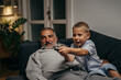 © cherryandbees - grandfather and grandson laying on the sofa and watching tv at home