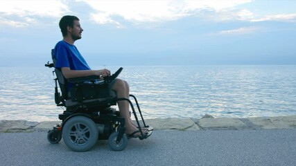 Wall Mural - Man on wheelchair near sea looking at sunset.