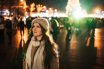 red-haired young woman stands on the street in the evening of new year and christmas waiting for the holiday, in the background there are many festive lights and lights