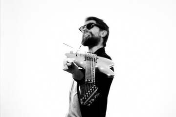 A man holds a guitar in his hands black leather jacket dark glasses music performance light background