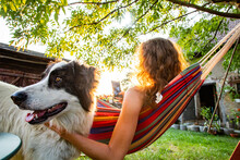 Woman With Dog Relaxing In Hammock In Back Yard