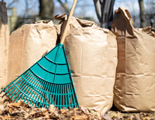 A Row Of Paper Leaf Composting Bags With A Leaf Rake Leaning On Them