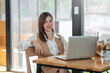© amnaj - Charming asian businesswoman sitting working on laptop. Looking at camera.