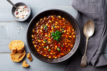 Wall Mural - Bean soup in a black bowl. Grey wooden background. Close up. Top view.