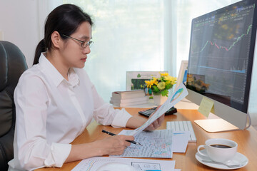 Business woman working in office with computer holding chart report paper and looking. business people analysis stock market, forex chart data on PC screen and paper. Business and finance concept.