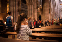 Girl In A Church Standing On Her Knees. Young Religious Woman In Glasses With Long Dark Hair, Praying In Catholic Cathedral.