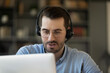 © fizkes - Close up of Caucasian male employee in headset look at laptop screen consult client customer online. Young man worker in earphones talk speak with web connection. Distant communication concept.