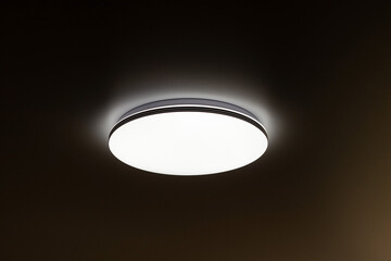 round flat lamp shines on the ceiling in the dark