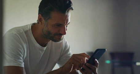 authentic close up shot of an young man is sitting on a bed and using a smart phone for send message