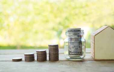 Bank note in jar with stack coin money and model house on wood with blur background. save future money for 2021 year buy a house with cash. not buy with loans.