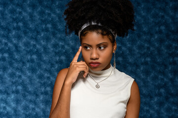 Wall Mural - Black Afro-Brazilian teenager with his finger close to his pensive face , on a blue background 