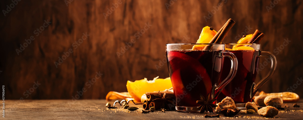 Hot mulled red wine cups with spices and fruits on wooden rustic table. Traditional Autumn hot drink, copy space - obrazy, fototapety, plakaty 