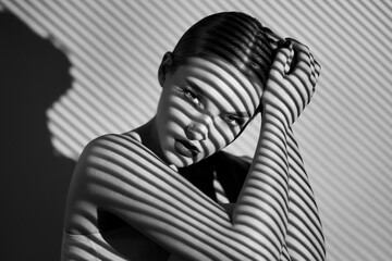 black and white portrait of a beautiful woman with a shadow pattern on the face and body in the form