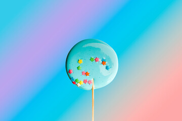 Hand made blue lollipop on wooden stick on  rainbow gradient background. The concept of sweets for the holidays, birthday. Candy bar. Flat lay. Copy space for text