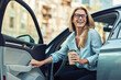 © Kostiantyn - Happy attractive woman or business lady wearing eyeglasses holding cup of coffee and getting out of her modern car
