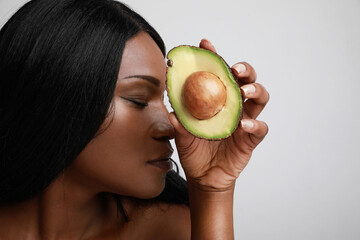 Wall Mural - Close-up portrait of afro young woman with avocado, healthy lifestyle. Posing over white background.