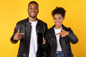 Black Couple Showing Smartphone With Blank Screen Over Yellow Background