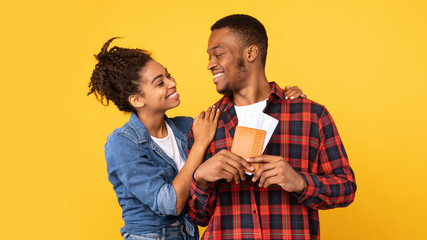 Happy Black Couple Hugging Holding Flight Tickets Over Yellow Background