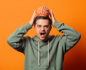 Wall Mural - Young surprising guy with a brain on orange background