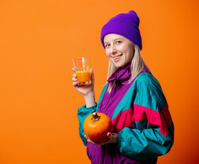 Pretty woman in 90s tracksuit with pumpkin juice on orange background