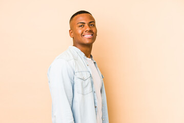 Wall Mural - Young latin man isolated on beige background looks aside smiling, cheerful and pleasant.