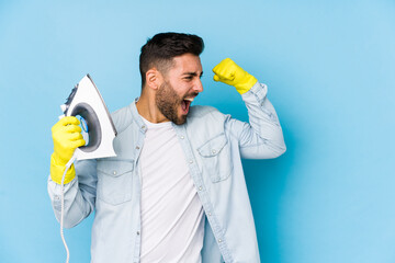 Wall Mural - Portrait of young man ironing isolated raising fist after a victory, winner concept.