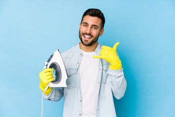 Wall Mural - Portrait of young man ironing isolated showing a mobile phone call gesture with fingers.