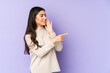 © Asier - Young indian woman isolated on purple background saying a gossip, pointing to side reporting something.