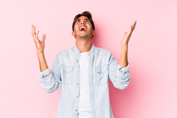 Wall Mural - Young caucasian man posing in a pink background isolated screaming to the sky, looking up, frustrated.