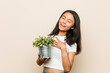 © Asier - Young asian woman holding a plant laughs out loudly keeping hand on chest.