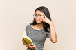 © Asier - Young asian woman student holding a book showing a disappointment gesture with forefinger.