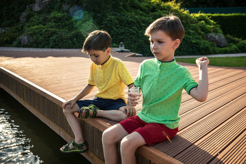 Wall Mural - Two children feed the wild ducks and shoal of small fish in azure clean transparent lake. Brother boys are best friends. Summer holiday friendship concept