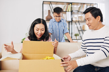 Poster - Cheerful woman opening big box she received from her husband and son for birthday