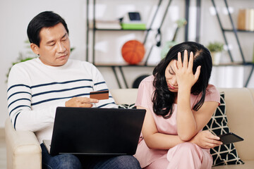 Poster - Upset mature couple sitting on sofa with laptop and credit card after spending all the money on paying bills