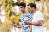 father gesturing and talking with teenager son in park