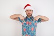 © Roquillo - Young caucasian man wearing hawaiian shirt and Santa hat over isolated white background pointing with two fingers at copy space down. Place for advertising