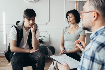 Pensive teenager sits next to his mother during a meeting with therapists for children with problems