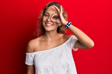 Beautiful caucasian woman wearing casual clothes over red background smiling happy doing ok sign with hand on eye looking through fingers