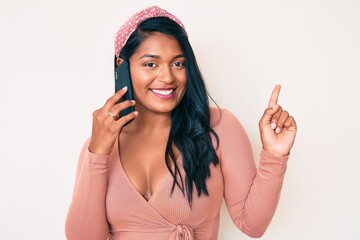 Wall Mural - Beautiful latin young woman with long hair having conversation talking on the smartphone smiling happy pointing with hand and finger to the side