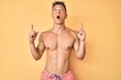 © Krakenimages.com - Young hispanic boy wearing swimwear shirtless amazed and surprised looking up and pointing with fingers and raised arms.