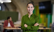 © Friends Stock - Portrait of a young beautiful female office worker keeping arms crossed, looking at camera and smiling while standing in the modern coworking space