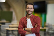 © Friends Stock - Portrait of a young cheerful caucasian male office worker looking at camera and smiling, keeping arms crossed while standing in the modern coworking space
