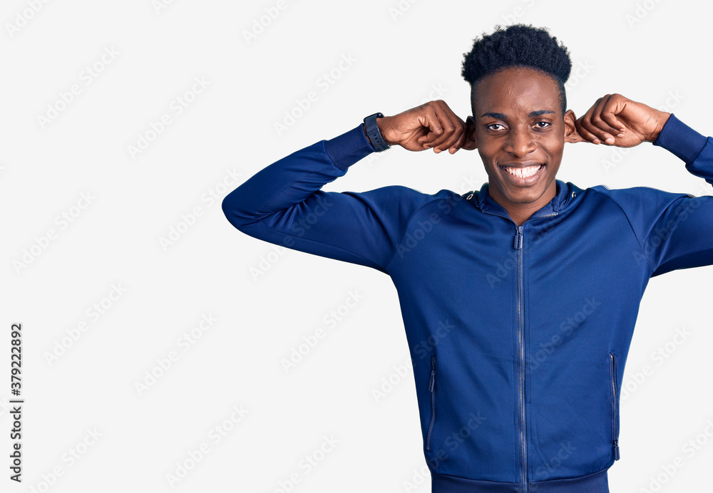 Young african american man wearing sportswear smiling pulling ears with fingers, funny gesture. audition problem