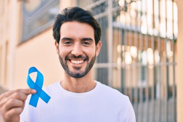 Young hispanic man smiling happy holding blue ribbon at the city.