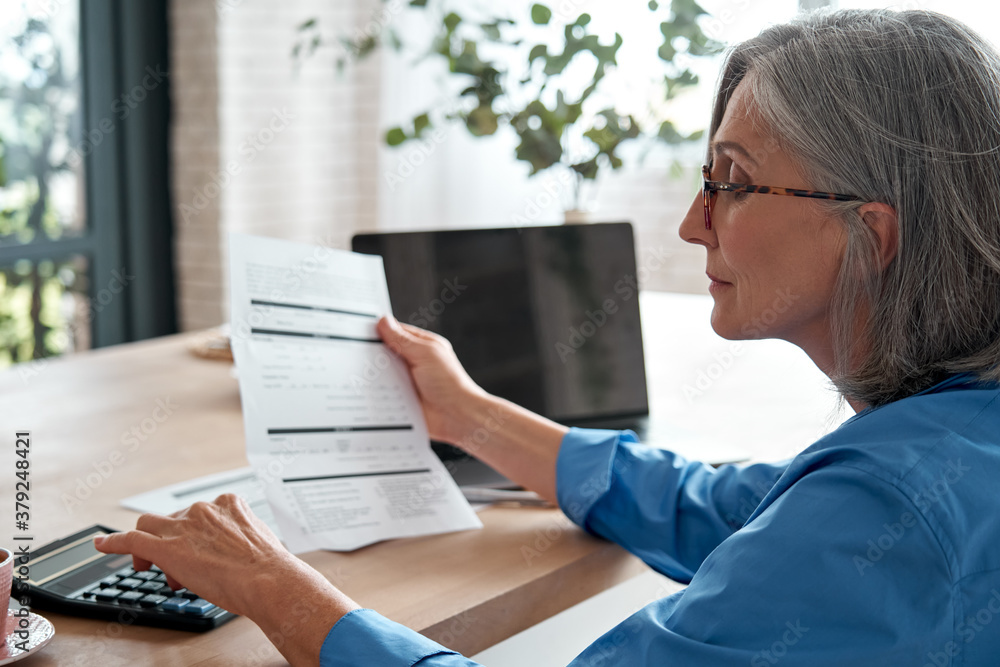 Senior mature business woman holding paper bill using calculator, old lady managing account finances, calculating money budget tax, planning banking loan debt pension payment sit at home office table. - obrazy, fototapety, plakaty 