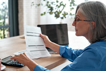 Senior Mature Business Woman Holding Paper Bill Using Calculator, Old Lady Managing Account Finances, Calculating Money Budget Tax, Planning Banking Loan Debt Pension Payment Sit At Home Office Table.