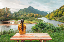 Camping Nature Woman Sitting At Picnic Table Enjoying View Of Wilderness River In Quebec And Autumn Foliage Forest, Canada Travel. Parc De La Jacques-Cartier, Quebec.